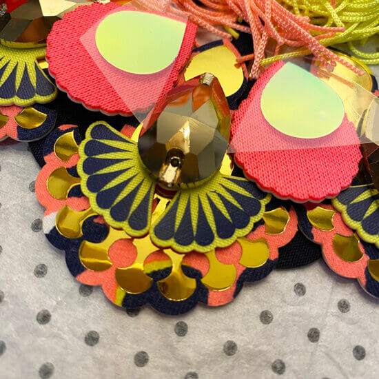 close up of a neon coral, navy and gold jewelled bib necklace with fluorescent fringe.