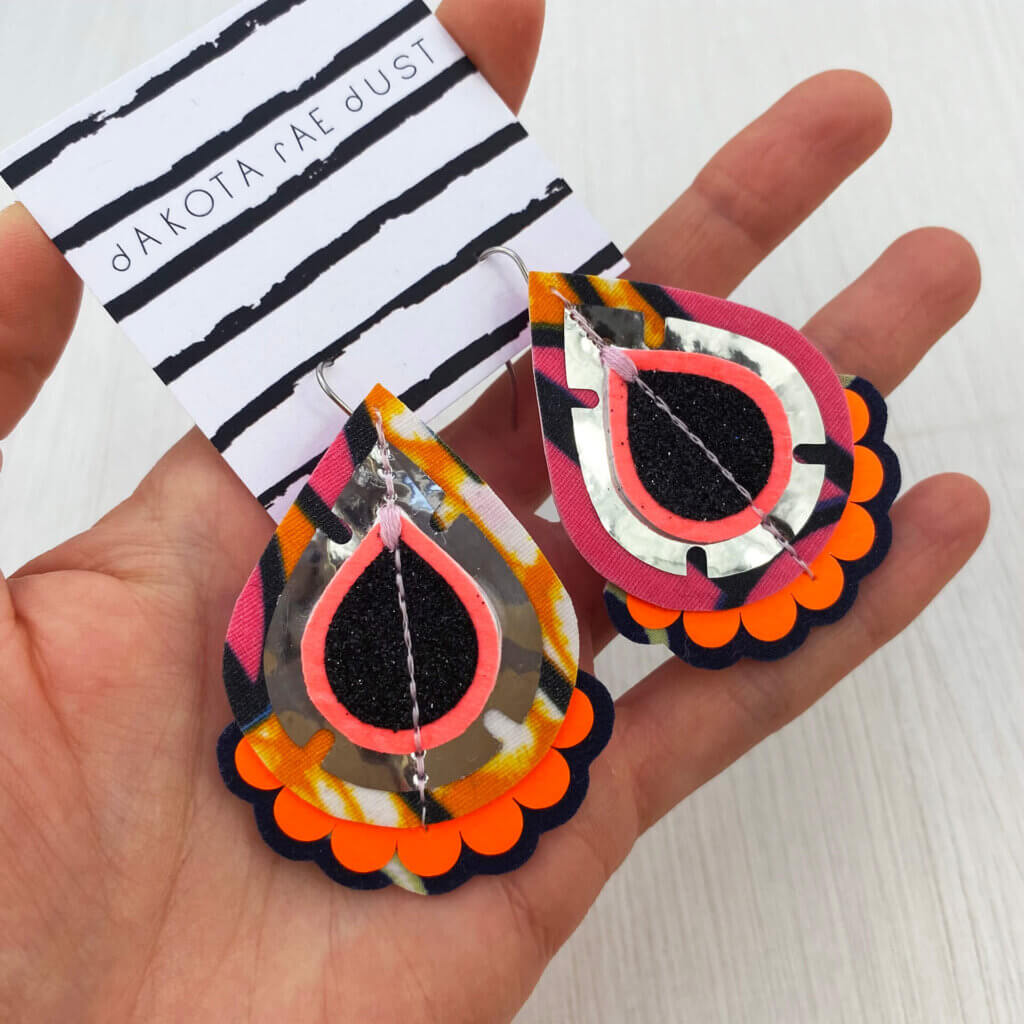 A pair of silver pink orange patterned fabric earrings held in a open hand