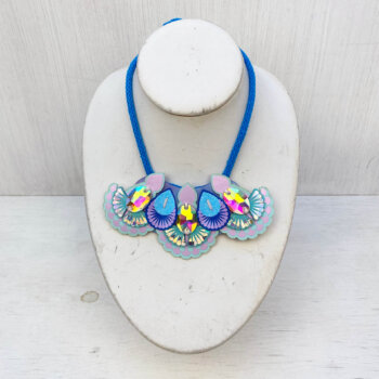 A light blue and lilac jewelled mini bib necklace is is displayed on an off white mannequin neck