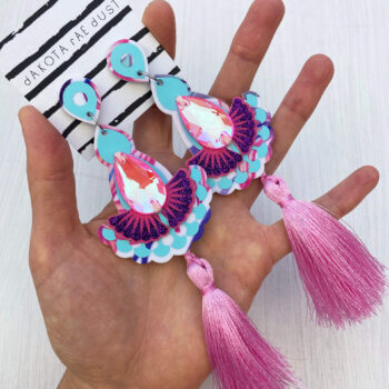 A pair of baby pink luxury tassel earrings are held in an open hand