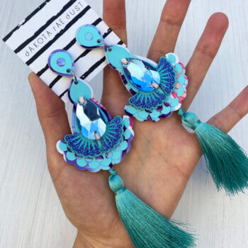 A pair of tropical blue luxury tassel earrings are held in an open hand
