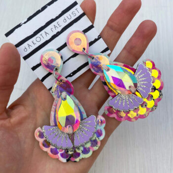 A pair of iridescent statement jewel earrings are held in an open hand